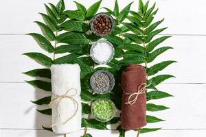 SPA still life with towel, different ingredients for body scrub and green leaves on a white wooden surface photo