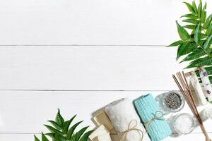 Spa set with towel and soap on white wooden background with green leaves photo