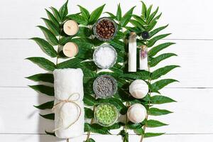 spa todavía vida con toalla, velas, diferente ingredientes para cuerpo fregar y verde hojas en un blanco de madera superficie foto