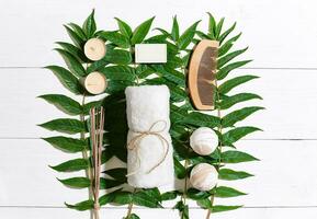 Spa set with towel and soap on white wooden background with green leaves photo