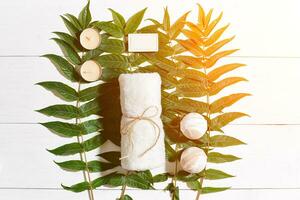 Spa set with towel and soap on white wooden background with green leaves. Sun flare photo