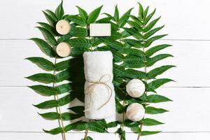 Spa set with towel and soap on white wooden background with green leaves photo