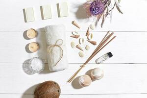 Spa set with sea salt, essential oil, soap and towel decorated with dry flower on white wooden background photo