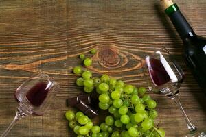 Red wine bottle, grape, chocolate and glasses over wooden table. Top view with copy space photo