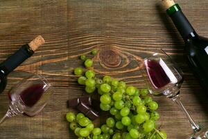 Bottles and glasses of wine, chocolate and ripe grapes on wooden background photo