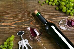 Red wine bottle, grape, chocolate and glasses over wooden table. Top view with copy space photo