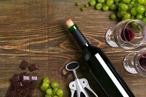 Red wine bottle, grape, chocolate and glasses over wooden table. Top view with copy space photo