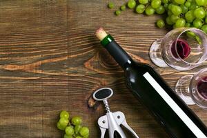 Red wine bottle, grape, chocolate and glasses over wooden table. Top view with copy space photo