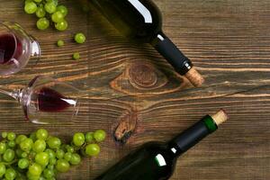 Red and white wine bottles, grape and glasses over wooden table. Top view with copy space photo