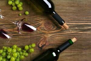 Red and white wine bottles, grape and glasses over wooden table. Top view with copy space photo