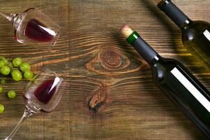 Red and white wine bottles, grape and glasses over wooden table. Top view with copy space photo