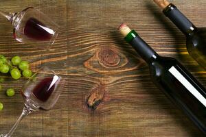 Red and white wine bottles, grape and glasses over wooden table. Top view with copy space photo