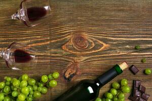 Red wine bottle, grape, chocolate and glasses over wooden table. Top view with copy space photo