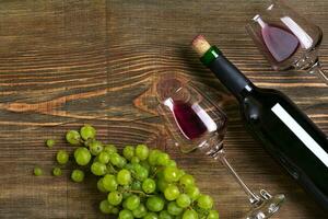 Red wine bottle, grape, chocolate and glasses over wooden table. Top view with copy space photo