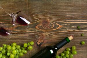 rojo vino botella, uva y lentes terminado de madera mesa. parte superior ver con Copiar espacio foto