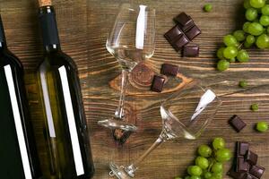 Red and white wine bottles, grape, chocolate and glasses over wooden table. Top view with copy space photo