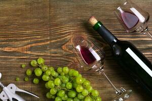 Red wine bottle, grape, chocolate and glasses over wooden table. Top view with copy space photo