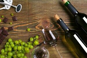 Bottles and glasses of wine, chocolate and ripe grapes on wooden background photo