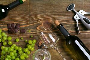 White wine bottle, grape, chocolate and glasses over wooden table. Top view with copy space photo