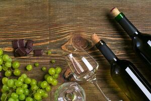 botellas y lentes de vino, chocolate y maduro uvas en de madera antecedentes foto