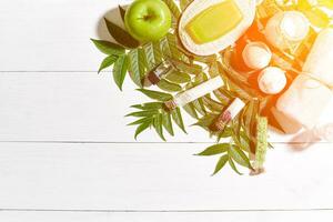 Spa set with towel and soap on white wooden background with green leaves. Sun flare photo