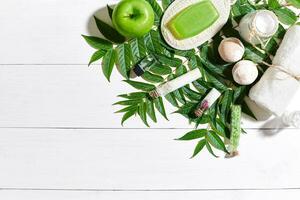 Spa set with towel and soap on white wooden background with green leaves photo