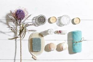 Spa set with sea salt, essential oil, soap and towel decorated with dry flower on white wooden background photo