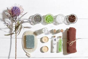 Spa set with sea salt, essential oil, soap and towel decorated with dry flower on white wooden background photo