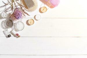 Spa set with sea salt, essential oil, soap and towel decorated with dry flower on white wooden background. Sun flare photo