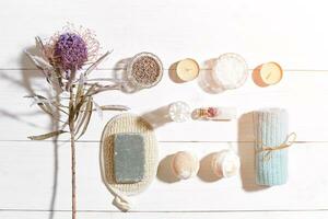 Spa set with sea salt, essential oil, soap and towel decorated with dry flower on white wooden background. Sun flare photo