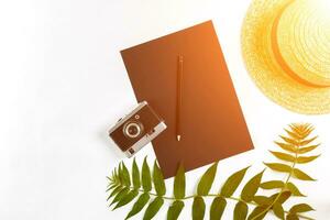 Straw hat with green leaves and old camera on white background, Summer background. Top view. Sun flare photo