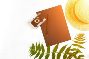 Straw hat with green leaves and old camera on white background, Summer background. Top view. Sun flare photo