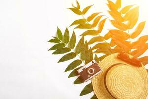 Straw hat with green leaves and old camera on white background, Summer background. Top view. Sun flare photo