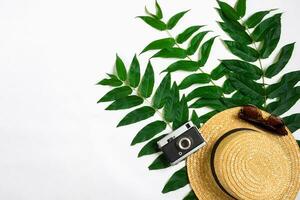 Straw hat with green leaves and old camera on white background, Summer background. Top view photo