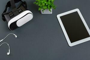 Virtual reality glasses and tablet with headphones on a gray background. Top view photo