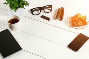 Modern workplace with digital tablet computer and mobile phone, cup of coffee and flower on white background. Top view photo