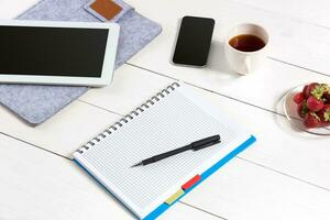 Office table desk with set of supplies, white blank notepad, cup, pen, tablet on white background. Top view photo