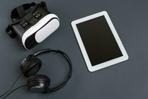 Virtual reality glasses and tablet with headphones on a gray background. Top view photo