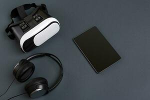 Virtual reality glasses and tablet with headphones on a gray background. Top view photo