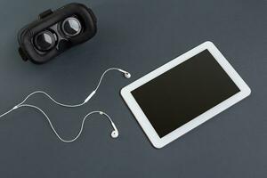 Virtual reality glasses and tablet with headphones on a gray background. Top view photo