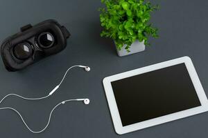 Virtual reality glasses and tablet with headphones on a gray background. Top view photo