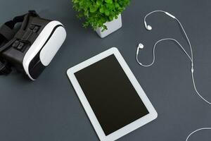 Virtual reality glasses and tablet with headphones on a gray background. Top view photo