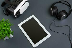 Virtual reality glasses and tablet with headphones on a gray background. Top view photo