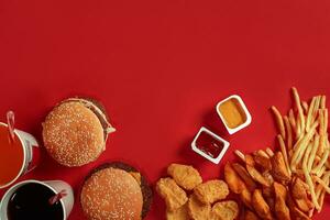 rápido comida plato parte superior vista. carne hamburguesa, patata papas fritas y vaso de bebida en rojo antecedentes. para llevar composición. foto