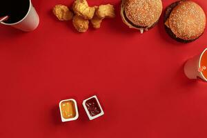 Fast food dish top view. Meat burger, potato chips and glass of drink on red background. Takeaway composition. photo