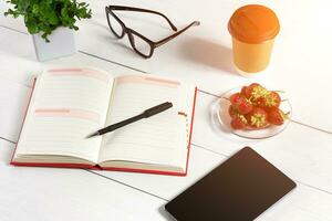 Office table desk with set of supplies, white blank notepad, cup, pen, tablet, glasses, flower on white background. Top view photo