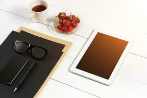 moderno lugar de trabajo con digital tableta computadora y móvil teléfono, taza de café, bolígrafo y vacío sábana de papel. foto