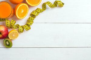 Fresh fruits with tape measure over white wooden background. Top view photo