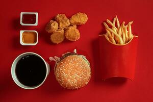 Concept of mock up burger, potatoes, sauce, chicken nuggets and drink on red background. Copy space for text and logo. photo