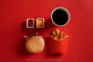 Concept of mock up burger, potatoes, sauce and drink on red background. Copy space for text and logo. photo